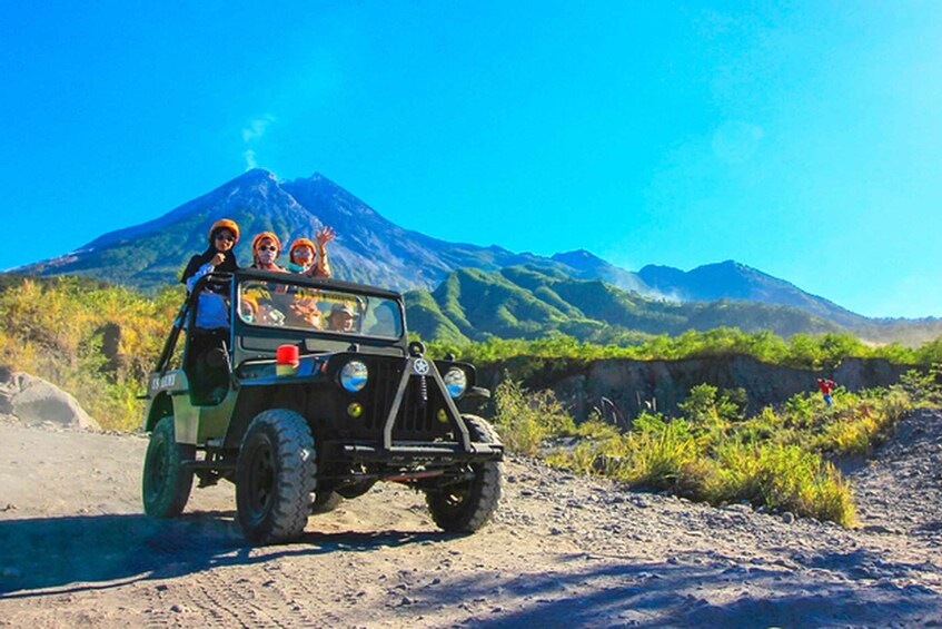 A jeep with passengers on a dirt road with a volcano in the background. 2