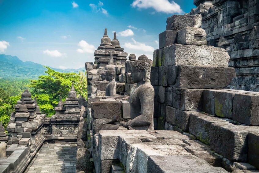 Ancient stone structures, including a seated Buddha statue, amidst lush greenery and mountainous terrain. 2