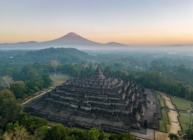 An ancient temple complex with a large pyramid structure, surrounded by lush greenery and a mountain in the background. 4
