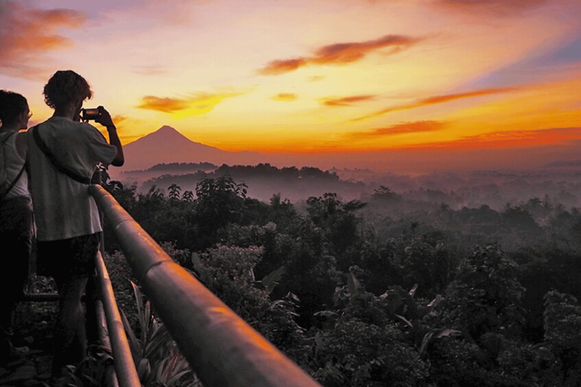 Two people taking a photo of a sunset with a mountain in the background. 3