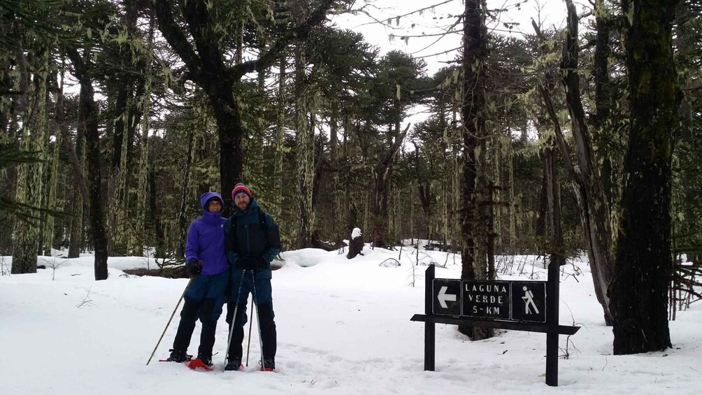 Two people in a snowy forest with a sign indicating Laguna Verde 5 km. 2