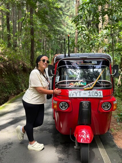 A person standing next to a red tuk-tuk on a forest road. 4