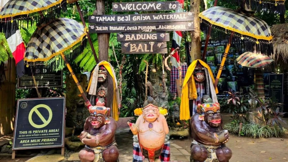 A private area with traditional Balinese statues and a sign welcoming to Taman Beji Griya Waterfall. 4