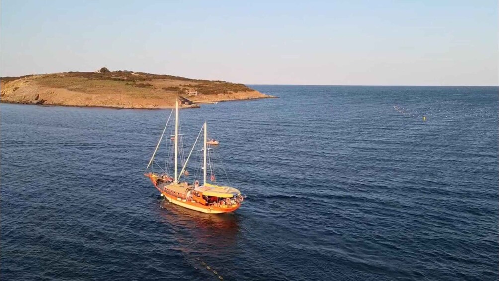 A sailboat on calm waters with a hilly coastline in the background. 1