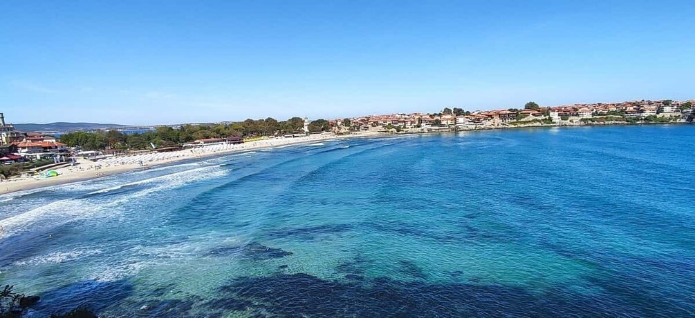 A coastal town with a clear blue sea, sandy beach, and buildings along the shore. 4