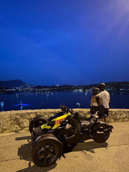 A motorcycle parked by a waterfront at dusk with a cityscape in the background. 5