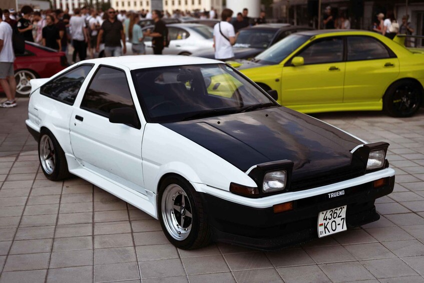 A white and black modified car with a custom license plate parked on a tiled surface. 4
