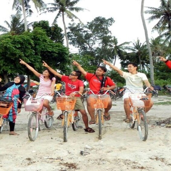 A group of people on bicycles with baskets, riding on a sandy path with palm trees in the background. 3