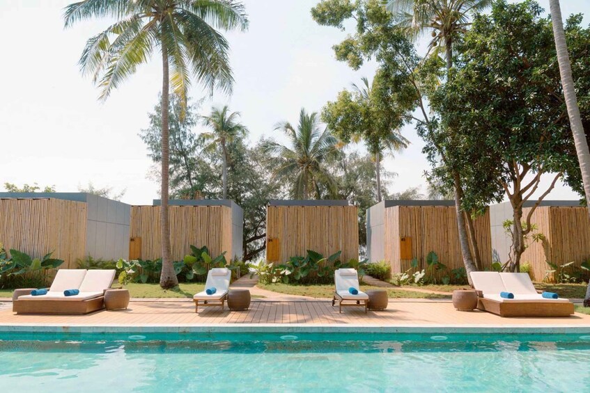 A poolside area with lounge chairs and wooden privacy screens, surrounded by palm trees. 4