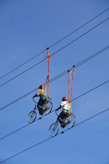 Two cyclists suspended in the air, riding bicycles attached to wires. 3