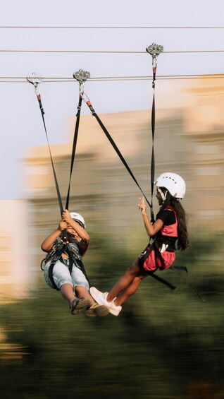 Two people ziplining, suspended by harnesses and ropes, with blurred background suggesting motion. 1