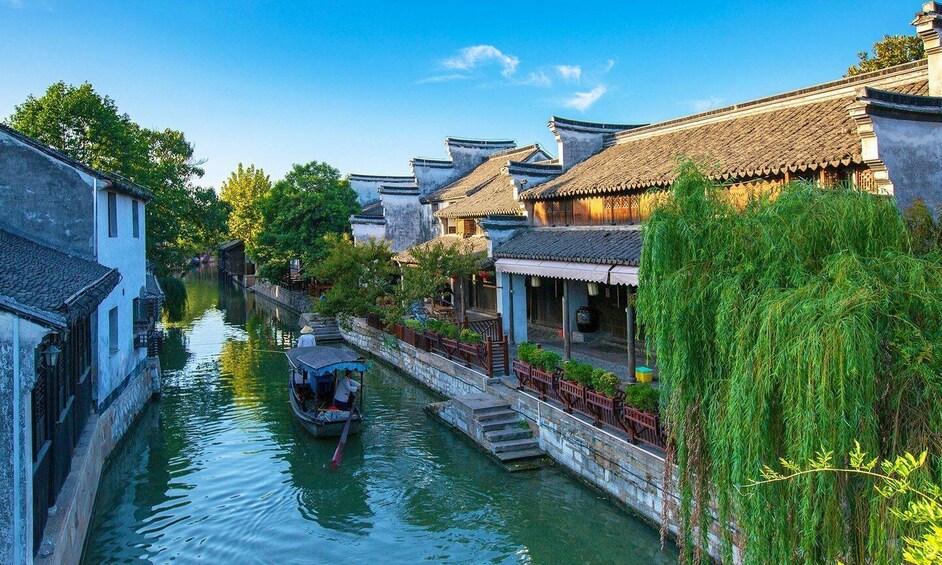 A traditional canal with buildings on either side, a boat with people, and lush greenery. 2