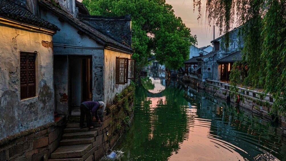 A narrow waterway flanked by traditional buildings with a person tending to a plant. 3