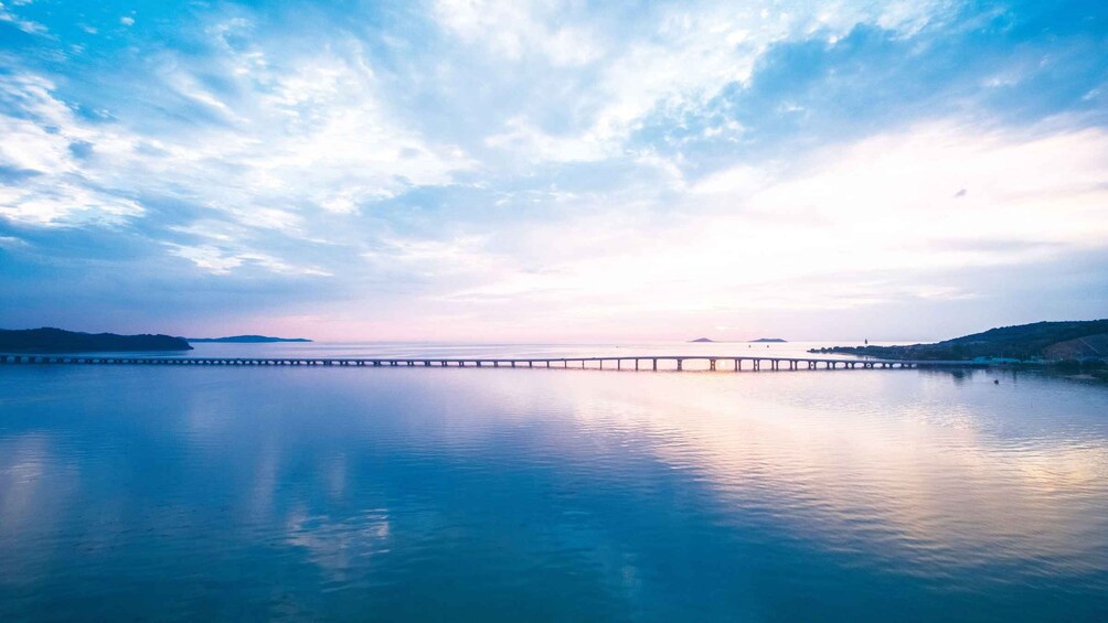 A calm lake with a pier extending into the water, surrounded by hills and a cloudy sky. 5