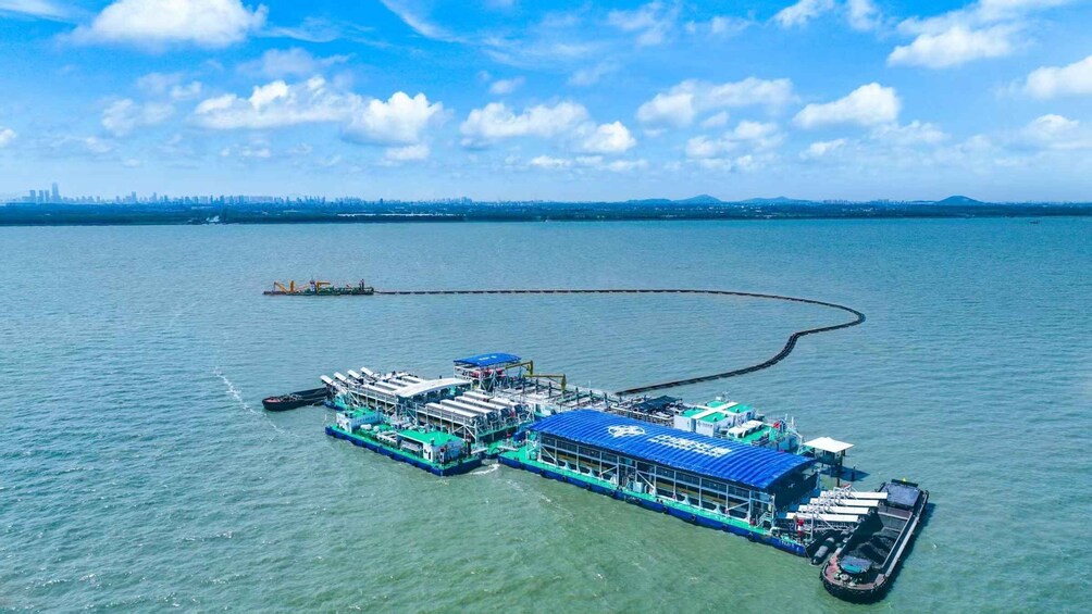 A floating structure with multiple decks and a docked boat, surrounded by calm water and a distant city skyline. 4