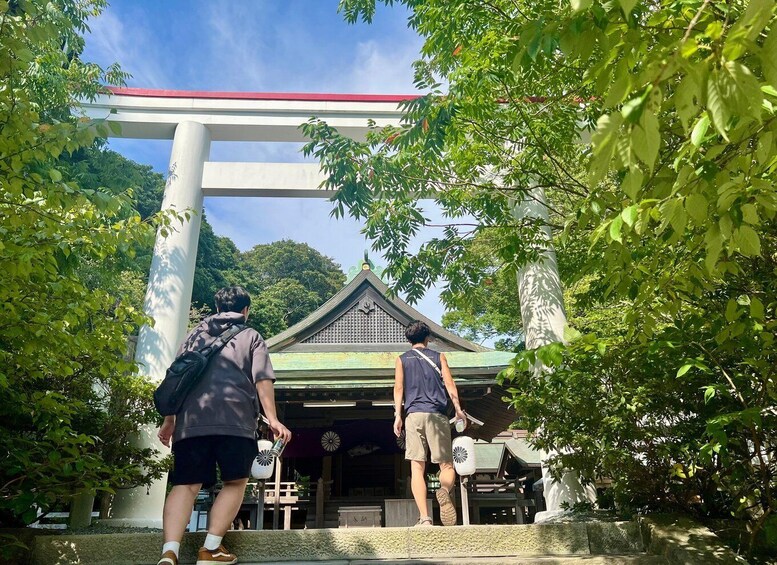 Two people walking towards a traditional Japanese building with a red roof, surrounded by lush greenery. 2
