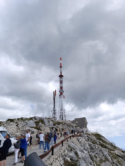 A telecommunications tower on a rocky hill with people walking around. 2