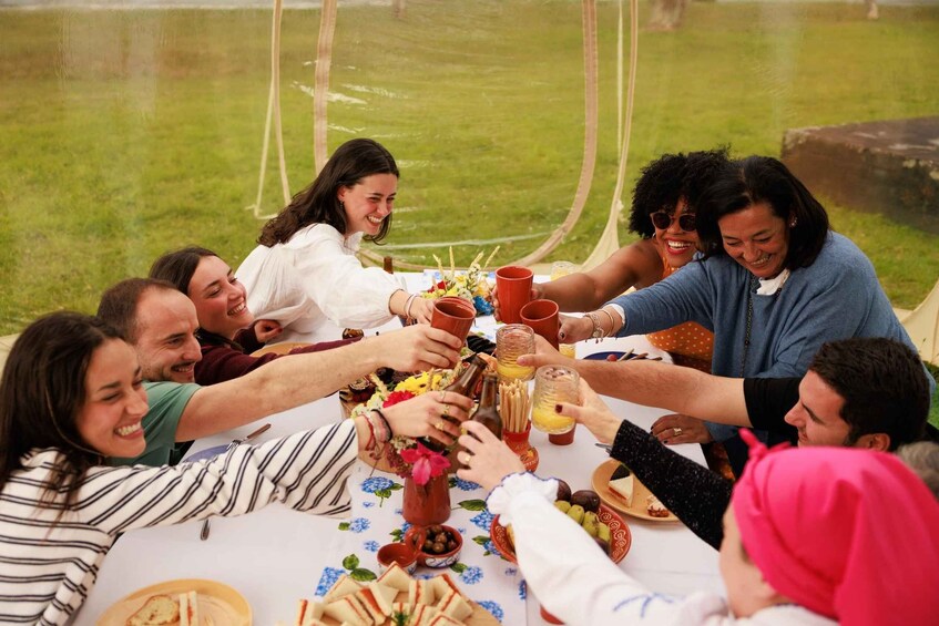 A group of people toasting around a table with food and drinks in an outdoor setting. 2