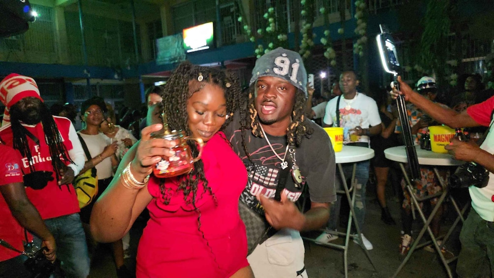 A group of people at an outdoor event, some holding drinks and others taking photos. 2