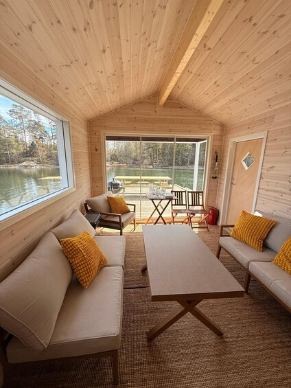 A wooden cabin interior with a large window overlooking a lake, furnished with sofas and a table. 1
