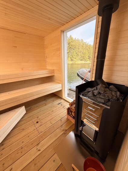 A sauna room with wooden walls, a black stove, and a window overlooking a lake. 2