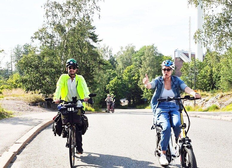 Two cyclists on a road with trees and a building in the background. 2