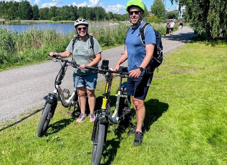 Two people on bicycles by a lakeside path with grass and trees. 1