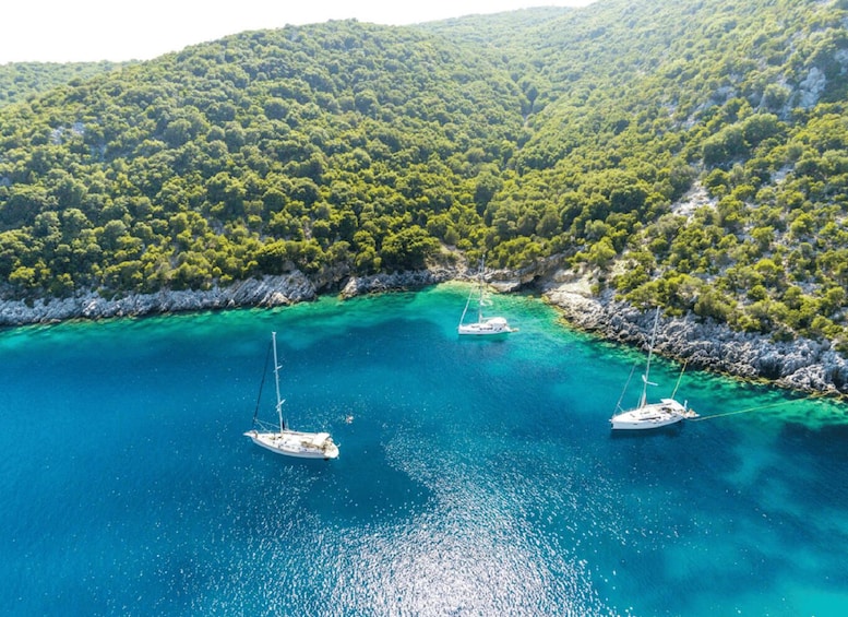 A coastal area with clear turquoise waters and three sailboats anchored near the shore. 2
