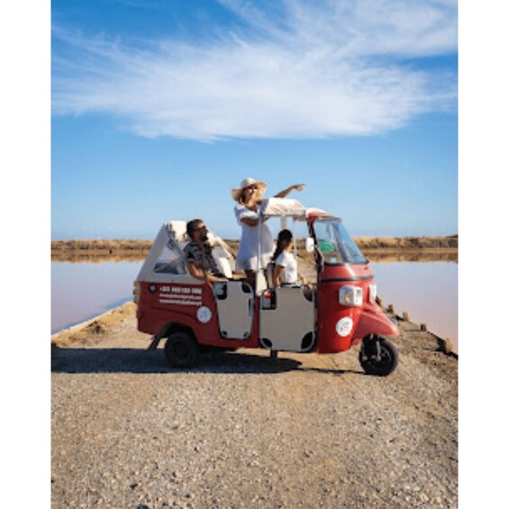 A red and white vehicle with passengers on a gravel path near a body of water. 3