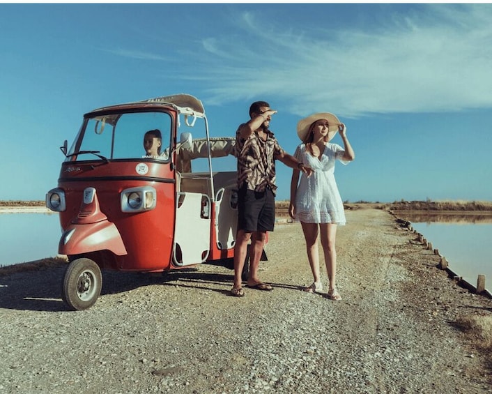 A vintage red car parked by a calm body of water, with a person standing beside it. 1