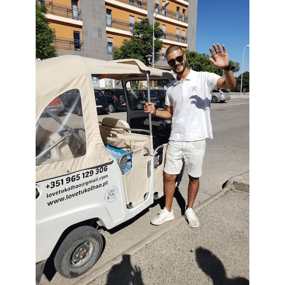 A man standing next to a white tuk-tuk with contact information on the side. 2