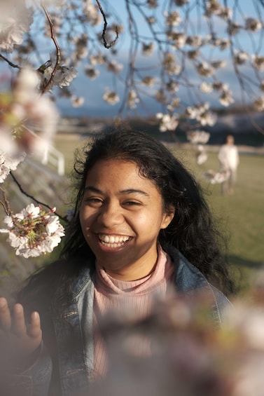 A person in a field with blooming trees and a distant figure in the background. 5