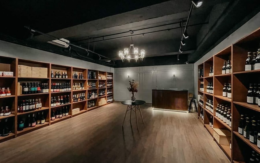 A dimly lit room with wooden shelves filled with bottles, a central table with a vase, and a chandelier. 5