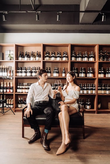 A man and a woman sitting on a leather couch in a wine cellar with shelves of wine bottles. 1