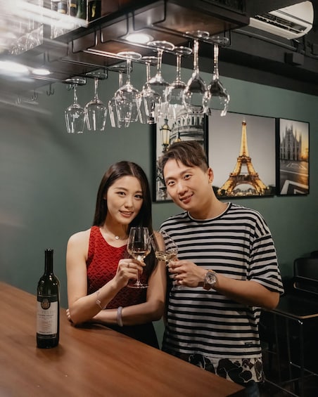 Two people holding wine glasses, a bottle of wine, and a wall with pictures of the Eiffel Tower. 3