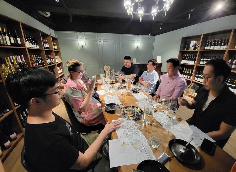 A group of people seated around a table in a wine cellar with shelves of wine bottles. 2