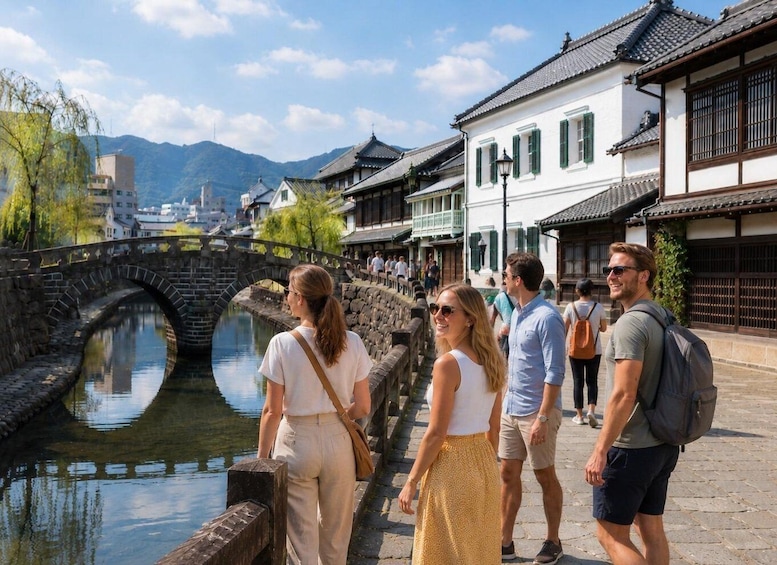 A group of tourists walking along a riverside path with traditional architecture and a stone bridge. 1