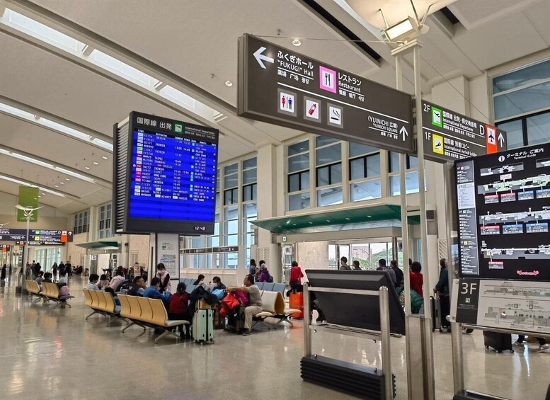 An airport terminal with seating areas, a flight information display, and directional signs. 4