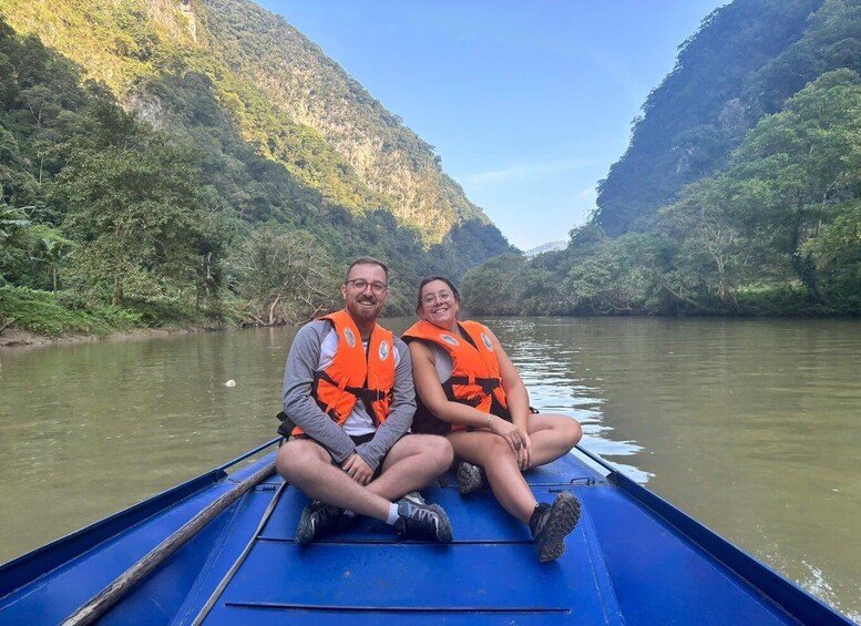 Two people in a blue boat on a river surrounded by green hills. 2