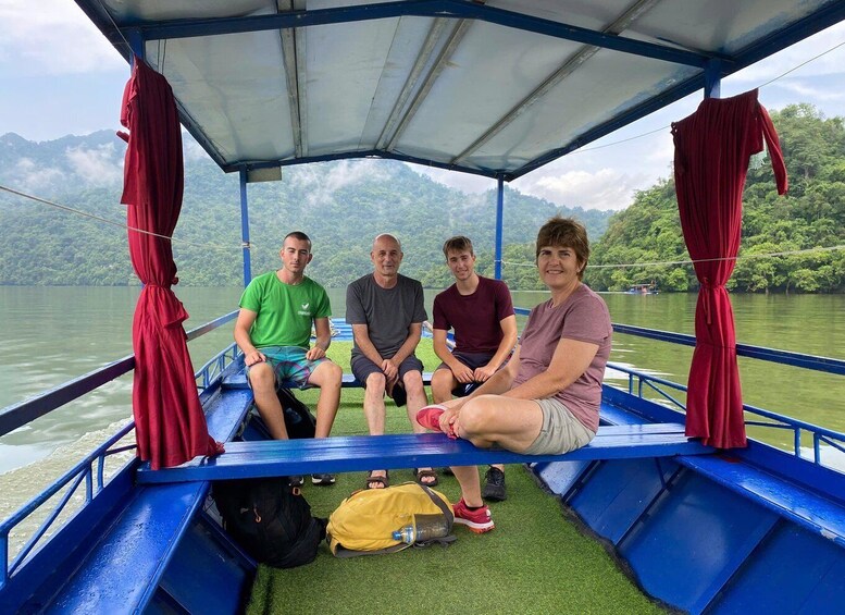 Four people seated on a boat with a blue railing, surrounded by water and greenery. 5