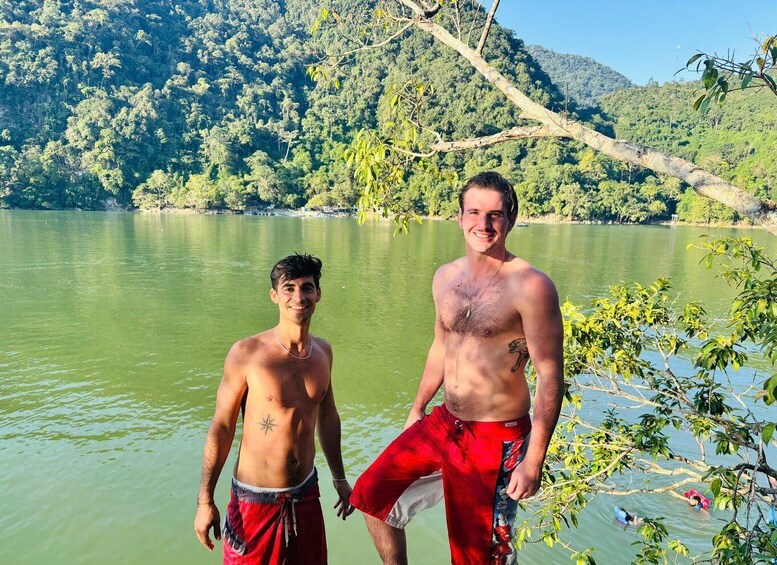 Two men standing by a lake with a forested hillside in the background. 4