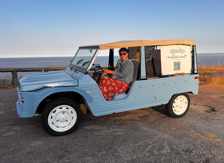 A vintage blue vehicle with a canopy, parked by a coastal road. 3