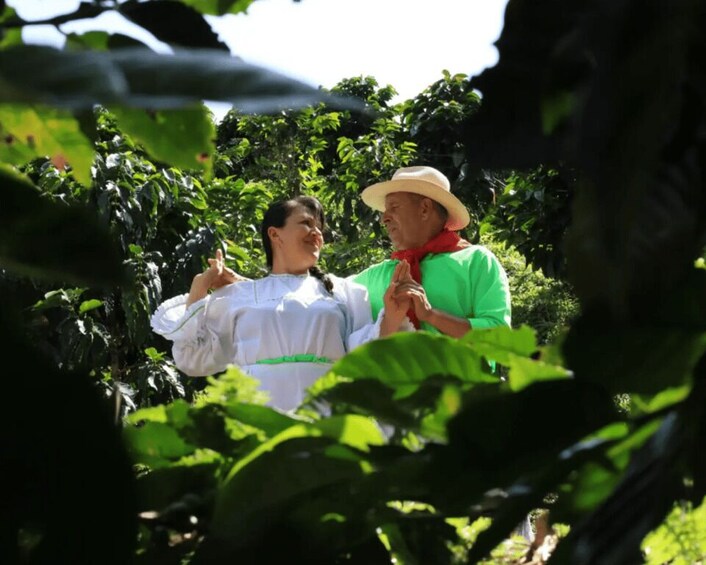 Two people in a lush garden, one wearing a white blouse and the other in a green shirt and hat. 1
