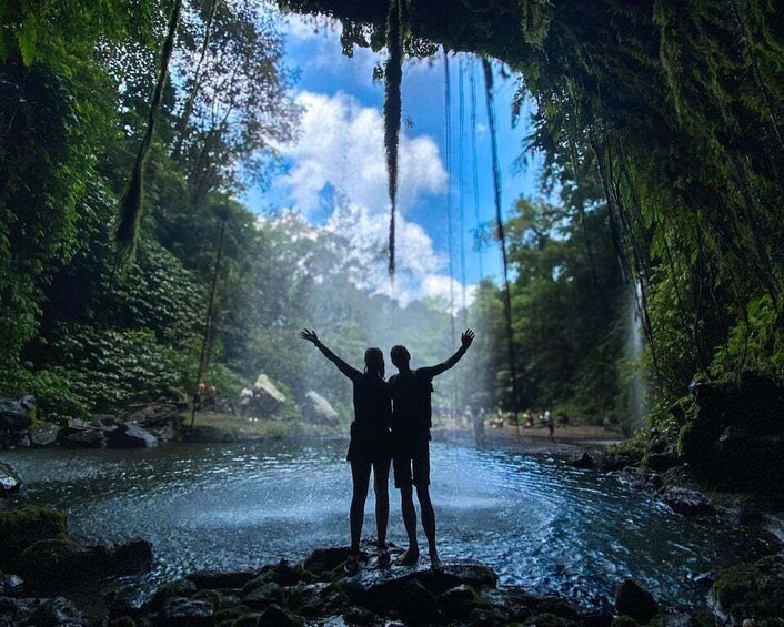 Two people standing by a waterfall in a forested area. 5