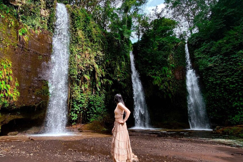 A woman in a dress standing in a forest with three waterfalls. 1