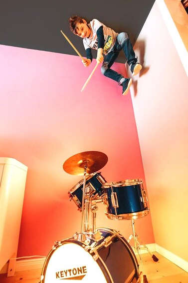 A child playing drums in a room with a pink wall and a drum set labeled 'KEYTONE.' 5