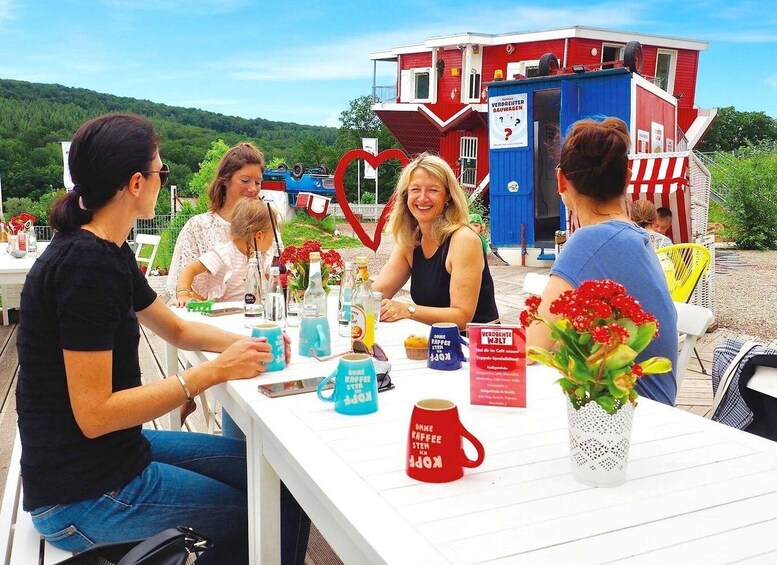 A group of people sitting at a table outdoors with a red building in the background. 3
