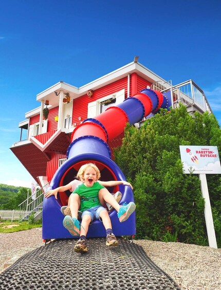 A child sliding down a colorful spiral slide in front of a red building. 2