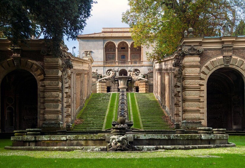 A classical fountain with statues, a staircase, and a building with arched windows in the background. 4