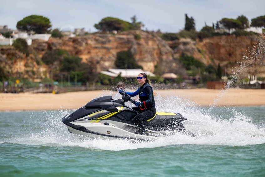 A person riding a jet ski on water with a beach and rocky cliffs in the background. 3